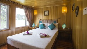 Une chambre bien éclairée avec un lambris en bois, un grand lit agrémenté de coussins turquoise, une table de chevet avec une lampe et une fen être avec des rideaux.