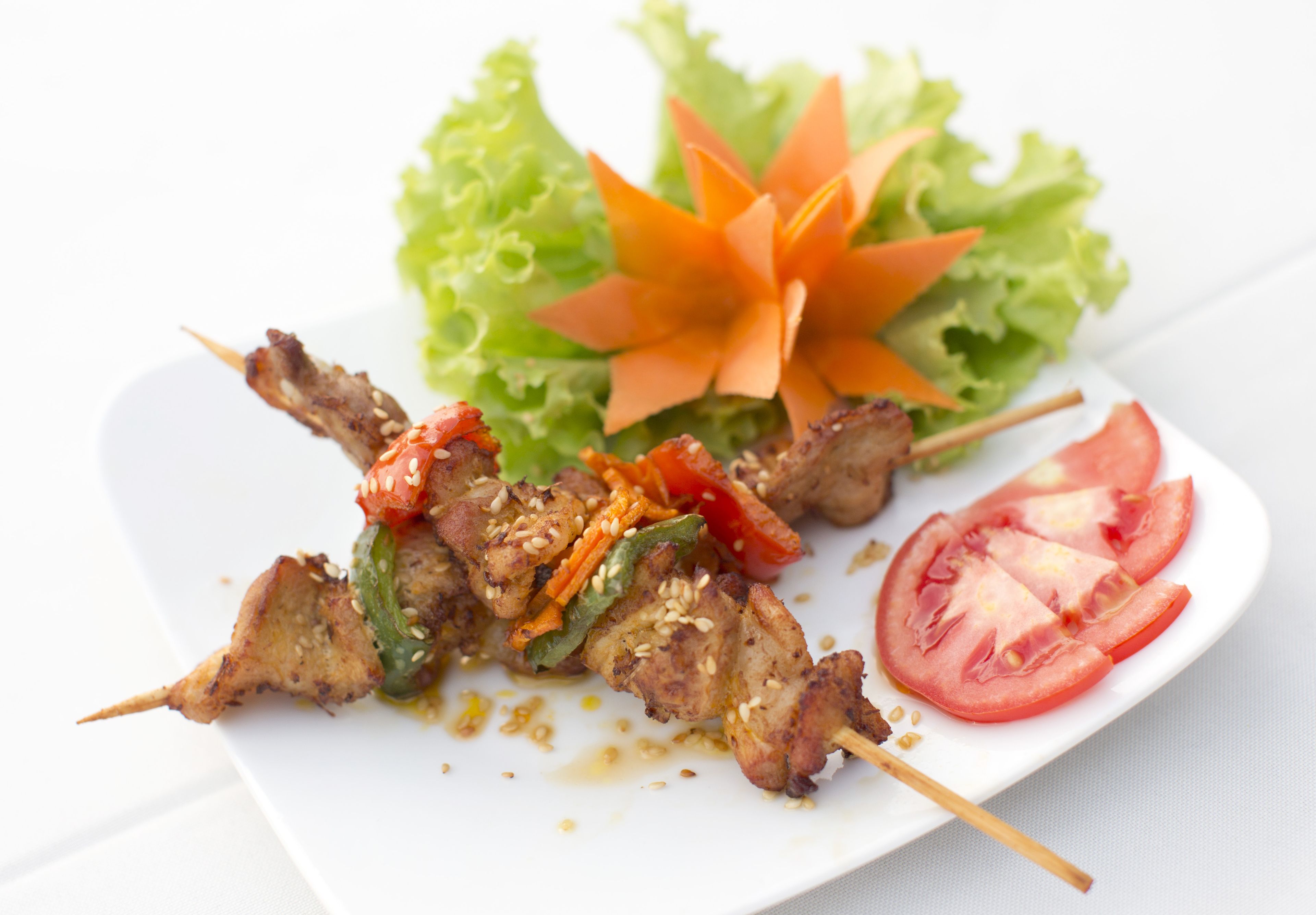 A plate of skewered meat with vegetables and a side salad.
