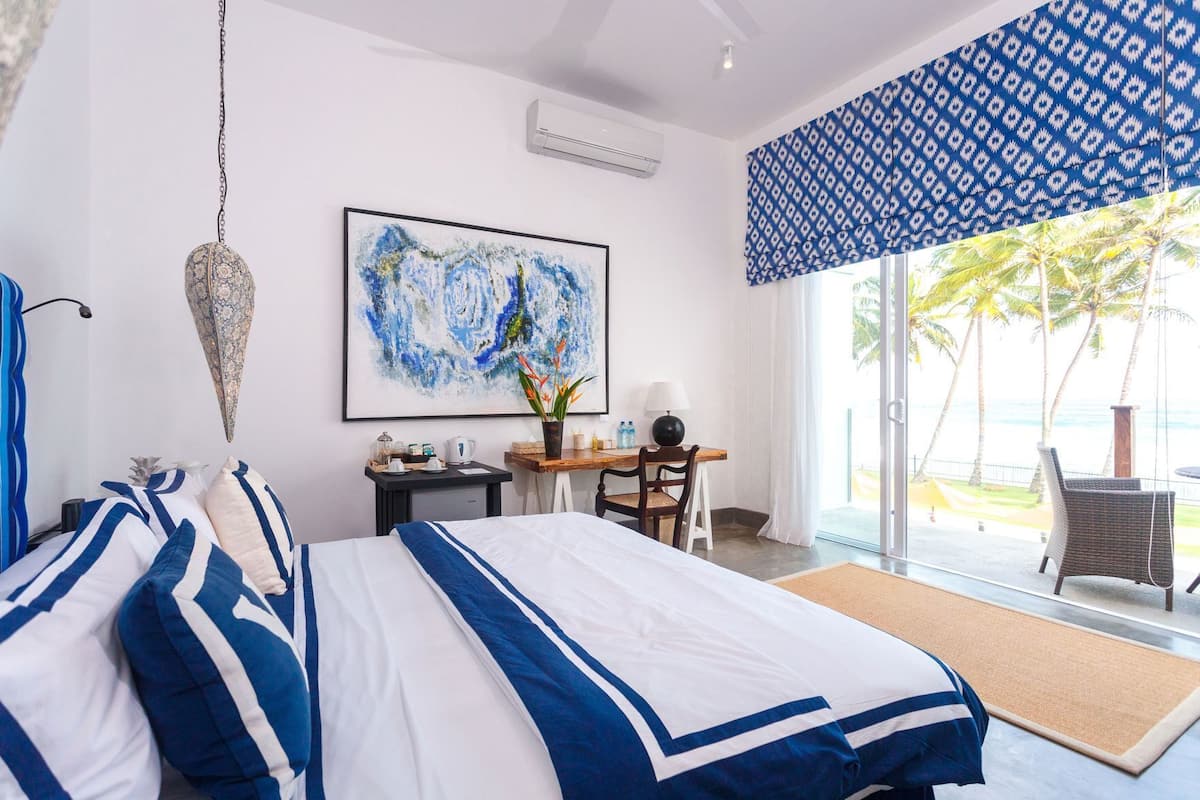 A hotel room with a bed, a desk, a chair, a large window with a view, and a hanging light fixture.