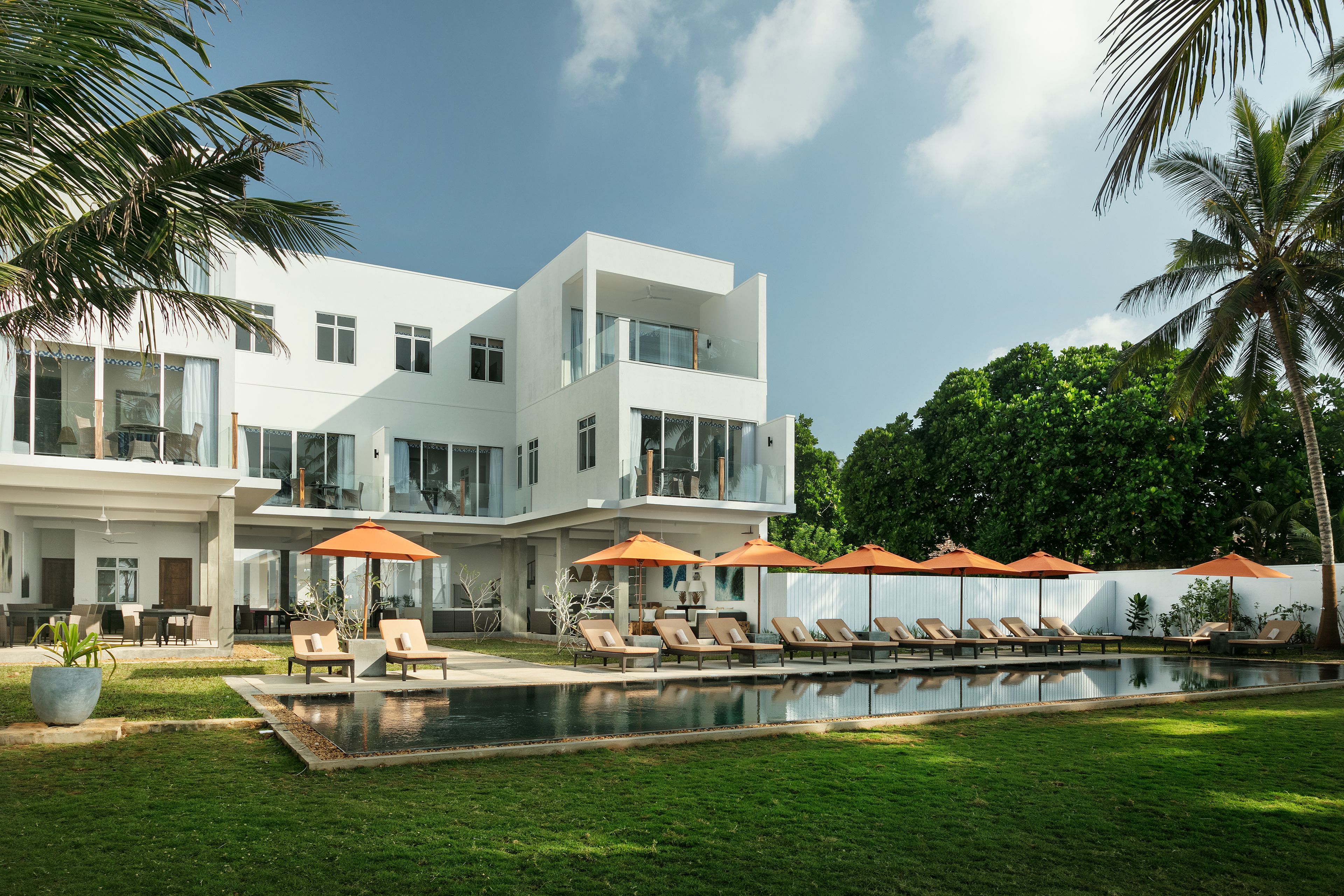A modern two-story house with a swimming pool, outdoor seating, and palm trees.