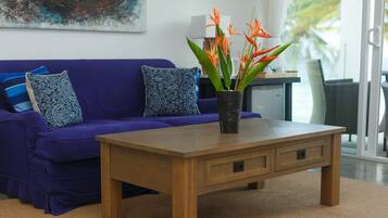 Una stanza con un divano viola, un tavolino in legno e una pianta in vaso con fiori arancioni.