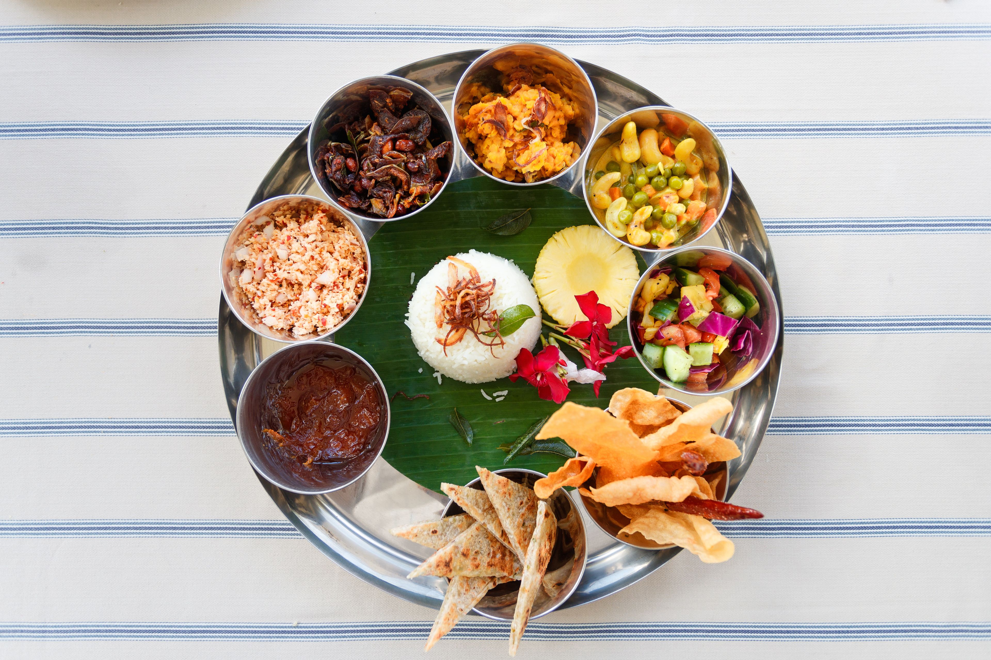 Comida tradicional del sur de la India servida en un plato de acero inoxidable y hoja de plátano, que incluye arroz, diferentes guisos y aperitivos.