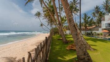 A beach with a wooden fence, palm trees, and a modern building with a pool.