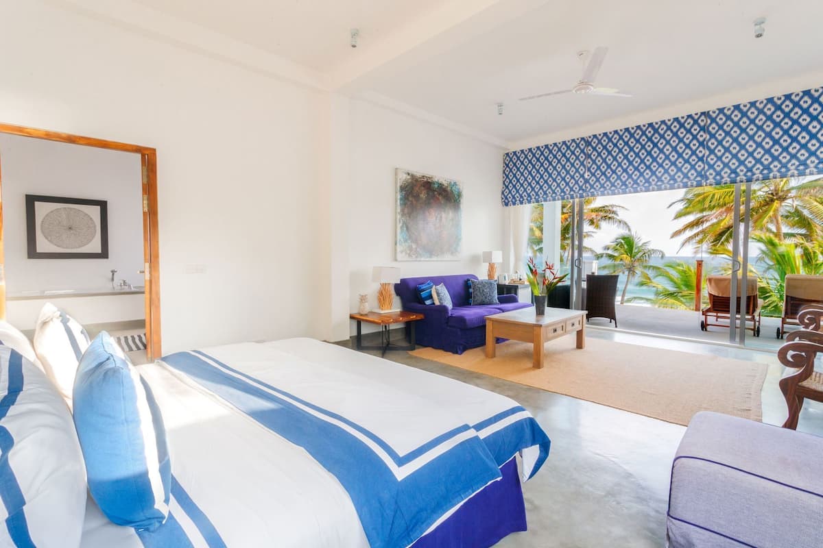 A bedroom with a bed, a sofa, a coffee table, and a view of the ocean.
