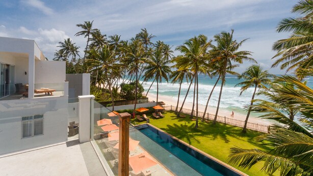 Un edificio moderno con piscina, palmeras y vista al mar.