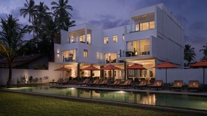 Un hotel moderno de varios pisos con piscina, mobiliario exterior y palmeras.