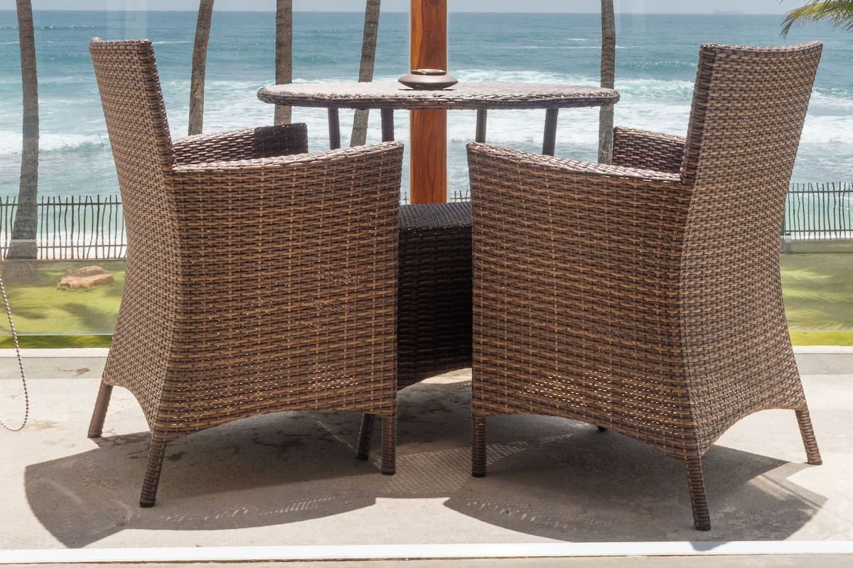 A wicker table and chairs set on a patio with a view of the ocean and palm trees.