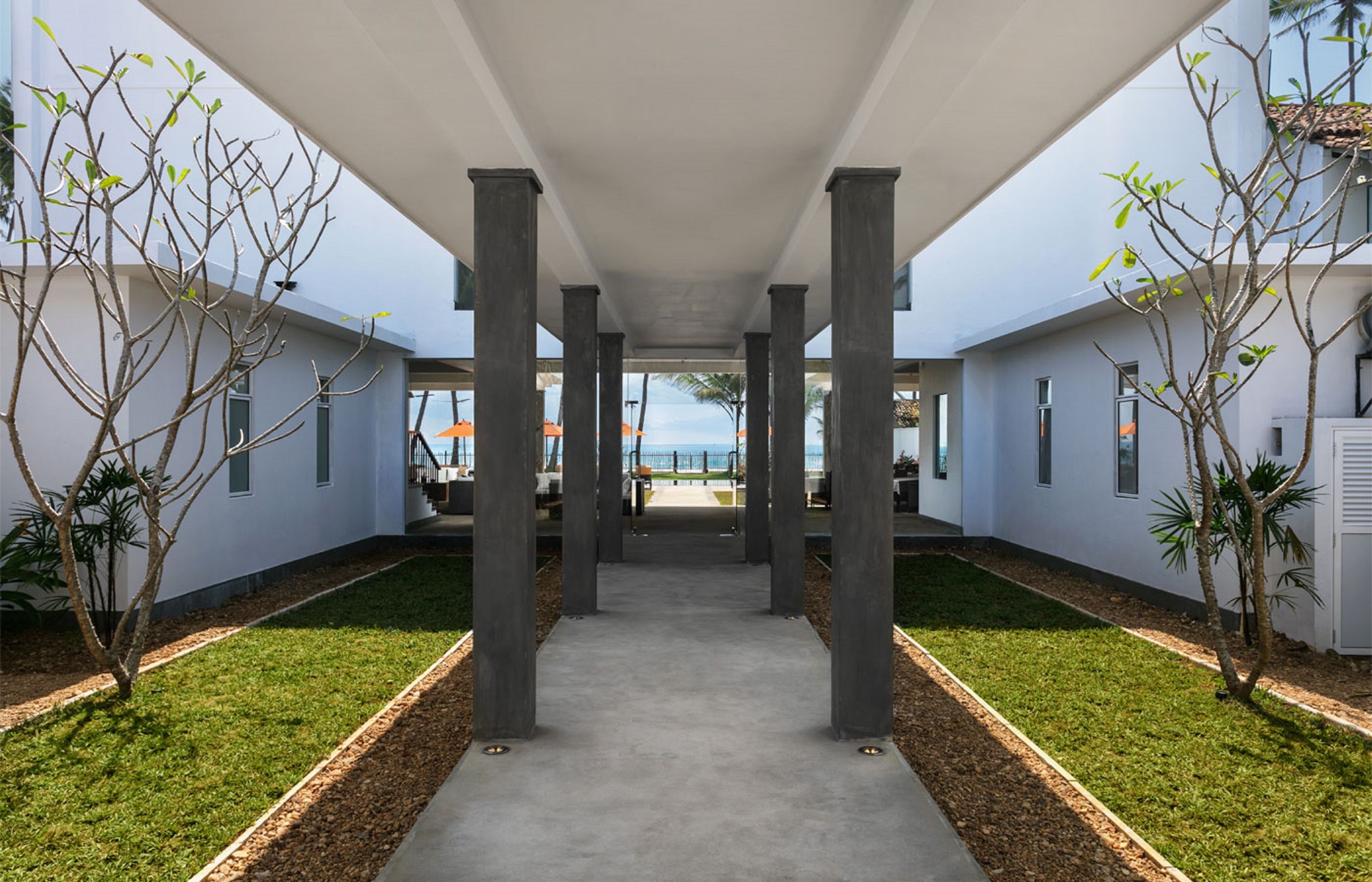 A covered walkway with columns, leading to a building with a view of the ocean.