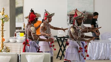 Un grupo de personas vestidas con atuendo tradicional realizan una danza en una sala con sillas blancas y una mesa decorada con arreglos florales.