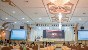 Une salle de conférence équipée d’un grand écran, de plusieurs tables et de chaises disposées pour une réunion.