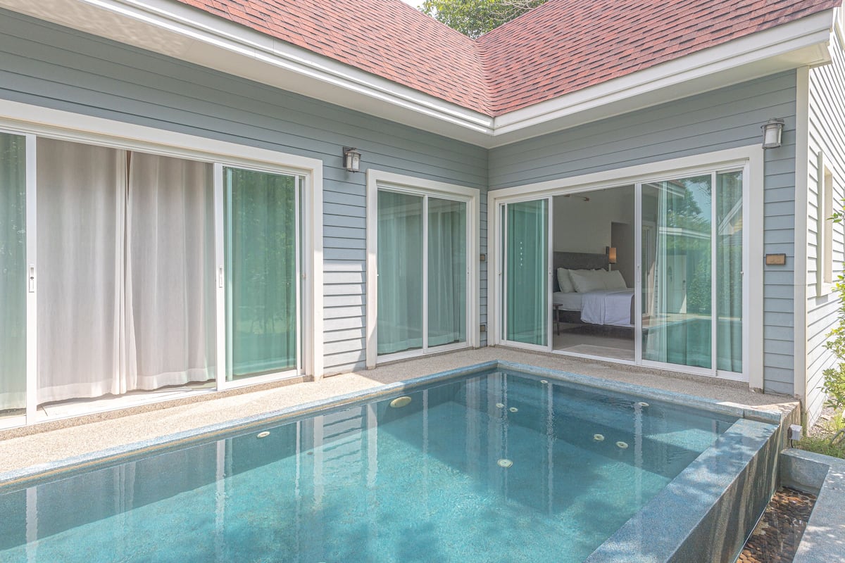 Une piscine située à côté d’une maison, avec de grandes portes-fenêtres coulissantes donnant accès à une chambre.