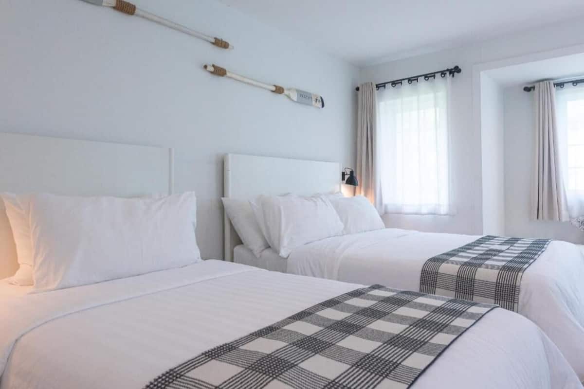 Deux lits avec du linge de lit blanc, une tête de lit et une couverture à carreaux.