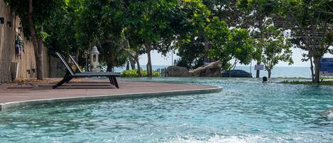 Una piscina con una tumbona, rodeada de árboles y vistas al mar.