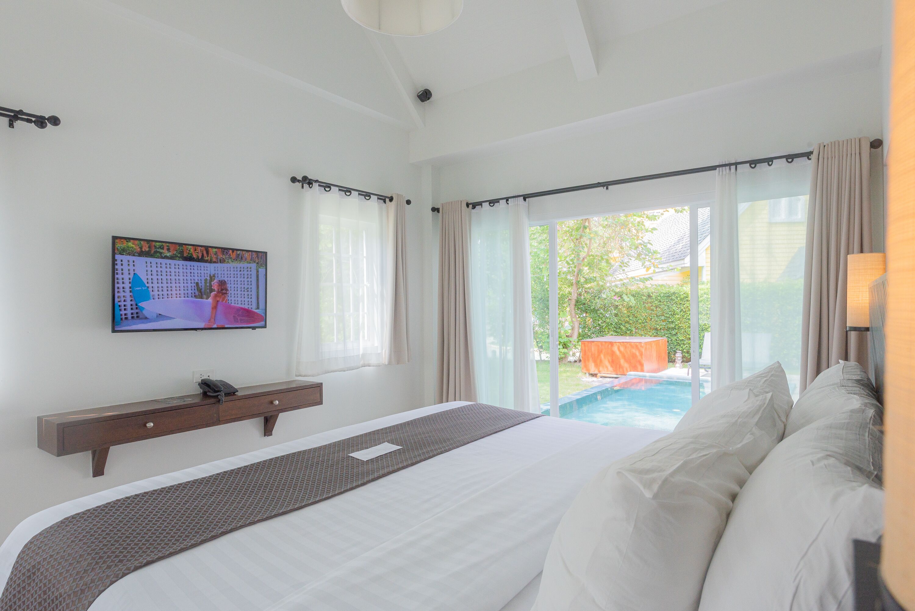 A hotel room with a bed, a TV on the wall, and a view of an outdoor swimming pool.