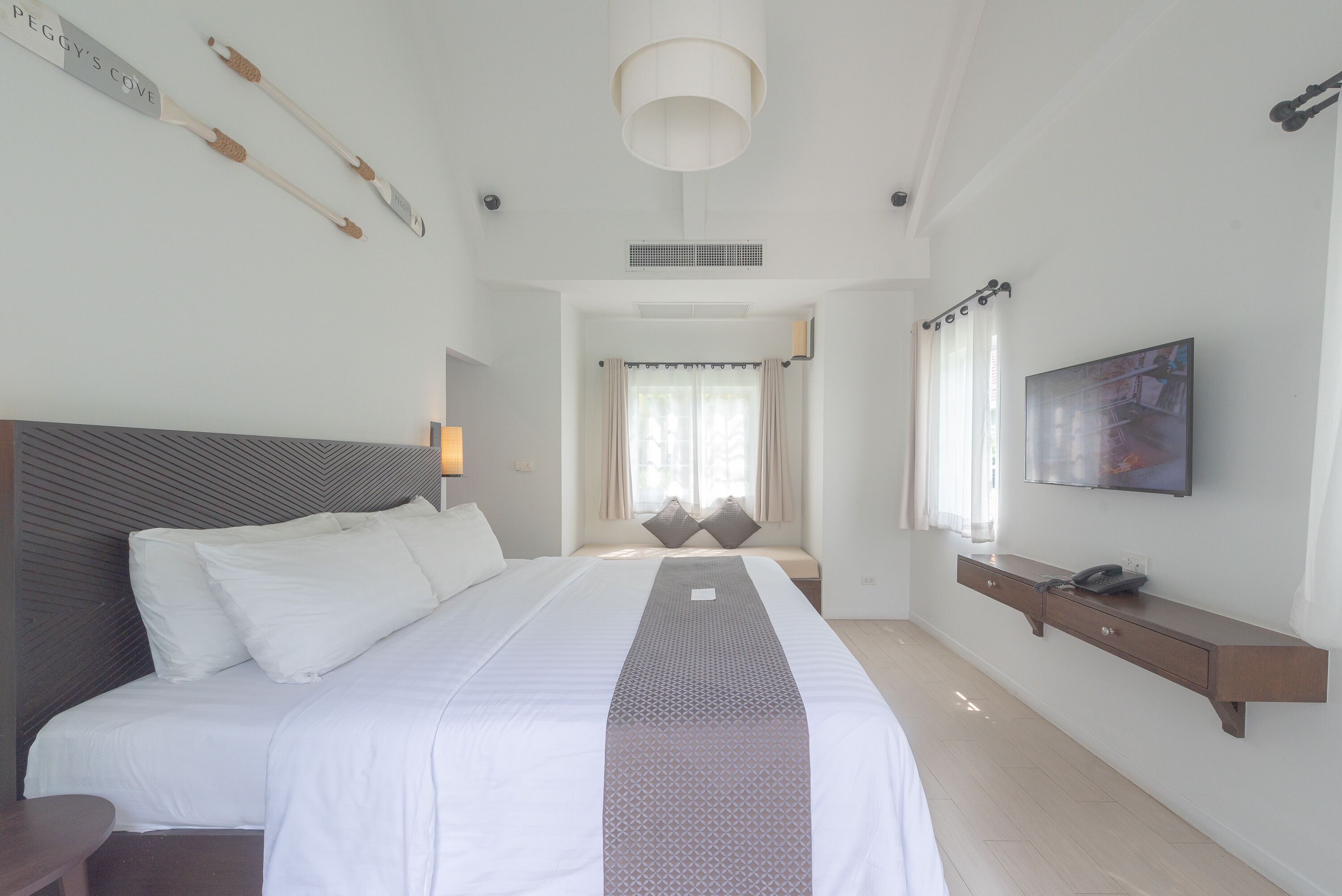 Una moderna camera d'albergo con un letto grande, un comodino, una TV a parete e una finestra con tende.