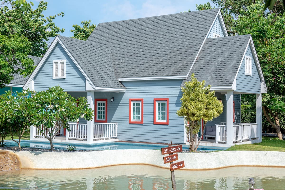 Une maison à deux étages, avec une façade bleue et des éléments décoratifs blancs, un porche à l’avant et une piscine.