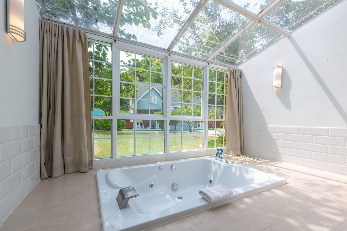 Une salle de bain moderne avec une grande baignoire, de grandes fenêtres et une vue sur une maison et la verdure environnante.