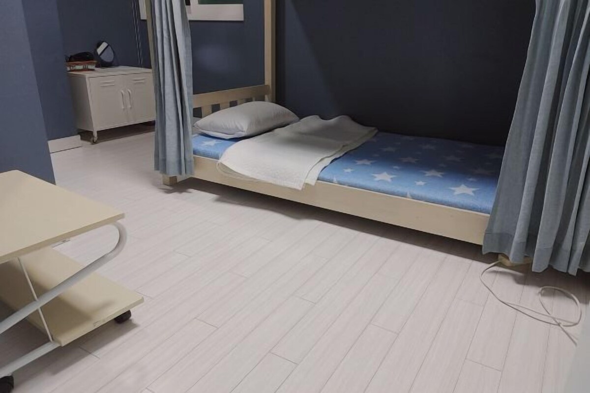 A bedroom with a single bed, a desk, and a nightstand.