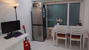 Cozinha compacta com geladeira, micro-ondas e área de refeições com mesa e cadeiras.