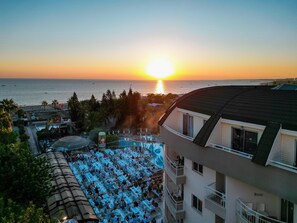 A resort with a pool area, a view of the sunset over the ocean, and a building with balconies. - Side Sun Hotel - All Inclusive (Manavgat)