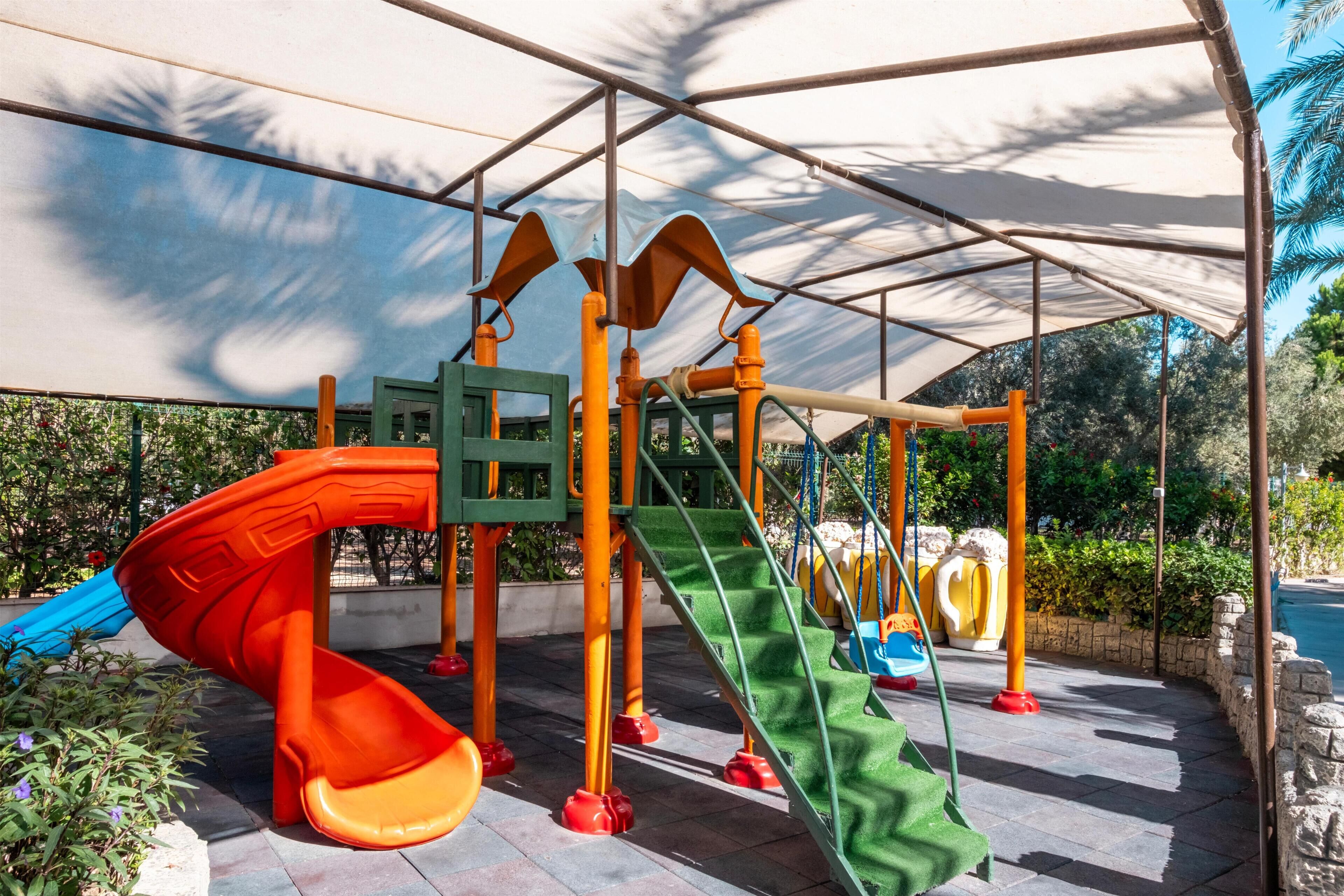 A playground with slides and climbing structures under a shaded canopy.