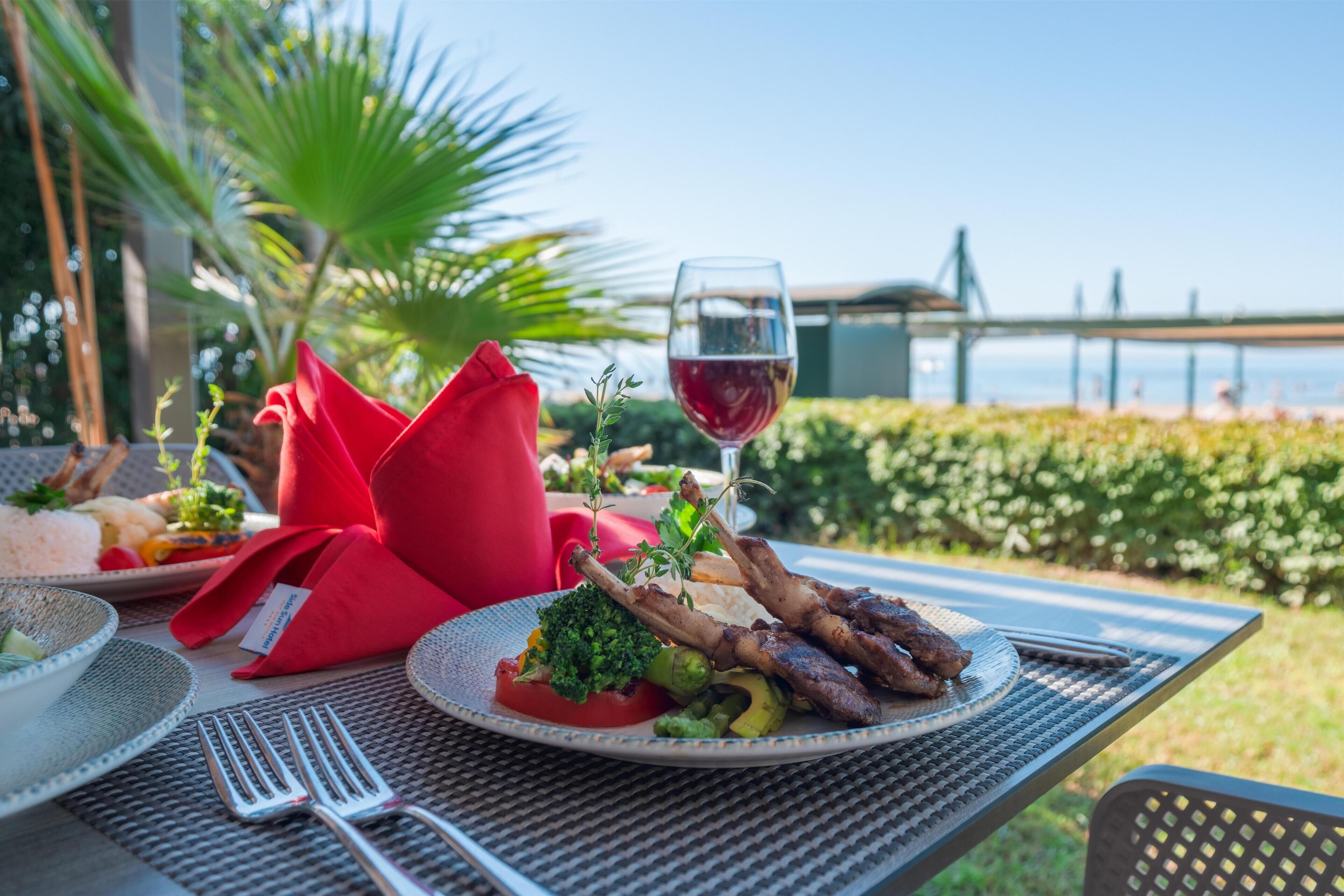 A table set outdoors with a meal, a glass of red wine, and a view of a bridge.