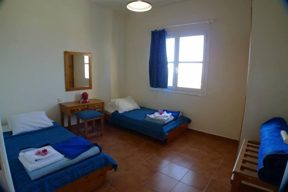 A small, clean room with two beds, a desk, and a window with curtains.