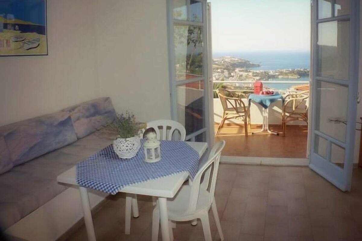 A balcony with a table and chairs, a sofa, and a view of the sea and town.
