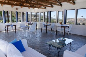 A covered outdoor seating area with white furniture and large windows offering views of the countryside. - Bellair Village (Malevizi)