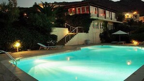 A swimming pool with a clear blue water surface, surrounded by lounge chairs and a staircase leading to a building with illuminated windows. - Bellair Village (Malevizi)