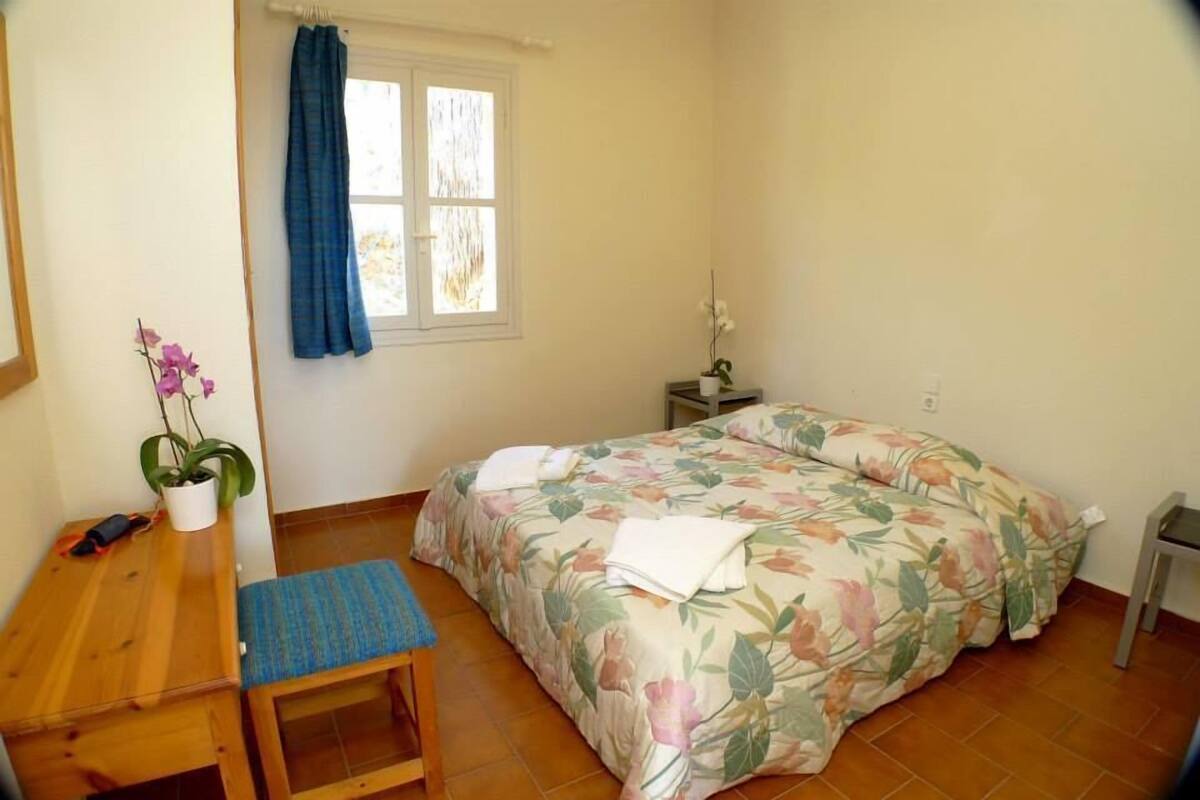 A bedroom with a bed, a small wooden table, a chair, a nightstand, and a window with curtains.