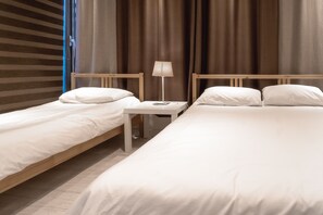 Een hotelkamer met twee eenpersoonsbedden, een klein nachtkastje met een lamp en een raam met gordijnen.