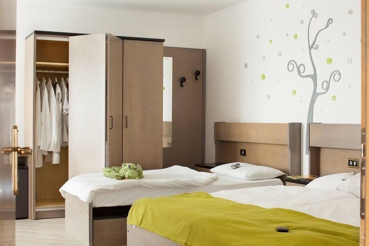 A hotel room with two beds, a wardrobe, and a wall with a tree decal.