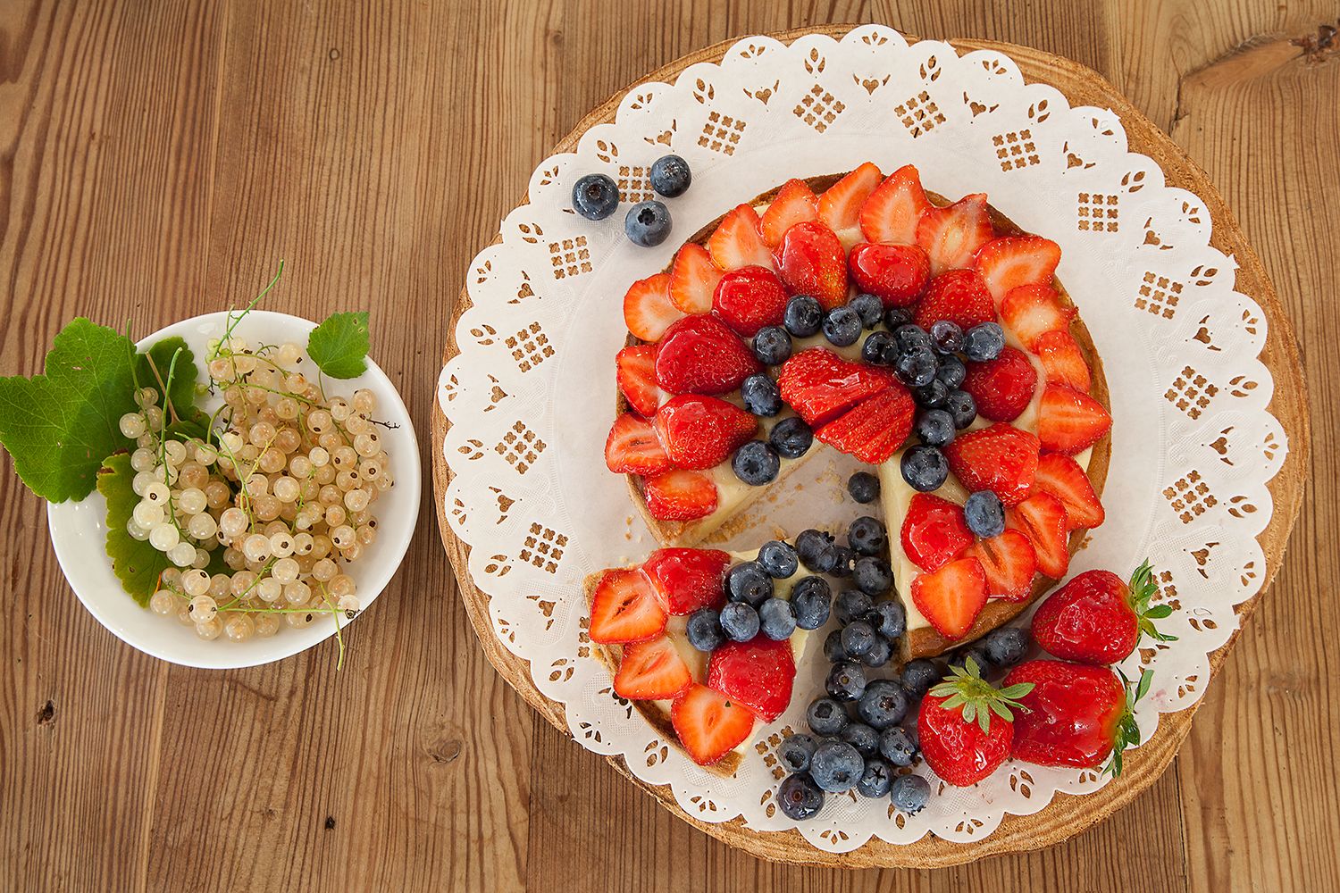 Una tarta de frutas redonda sobre una mesa de madera con un mantel de encaje.