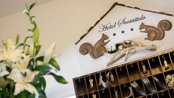 Un cartel de hotel con un zorro y una ardilla, un perchero de madera debajo y un arreglo floral a la izquierda.