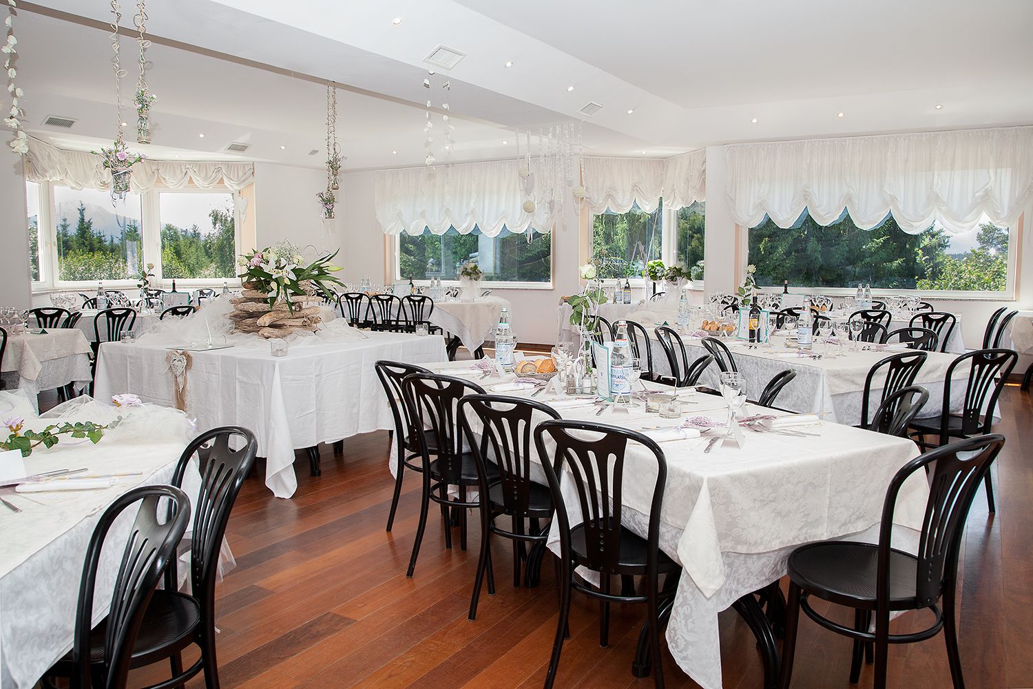 A restaurant with multiple tables set for dining, featuring white tablecloths and black chairs.