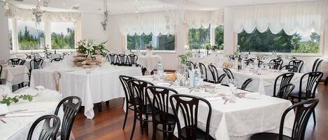 A restaurant with multiple tables set for dining, featuring white tablecloths and black chairs.