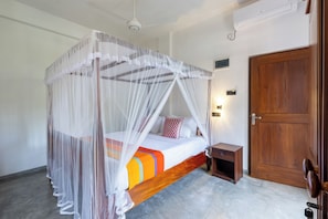 A room with a bed under a canopy, a bedside table, a wooden door, and a wall-mounted light.