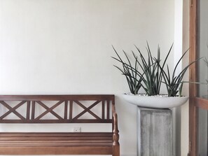 A wooden bench with a geometric backrest, a potted plant with long, narrow leaves, and a white wall. - Hanthana House (Kandy)