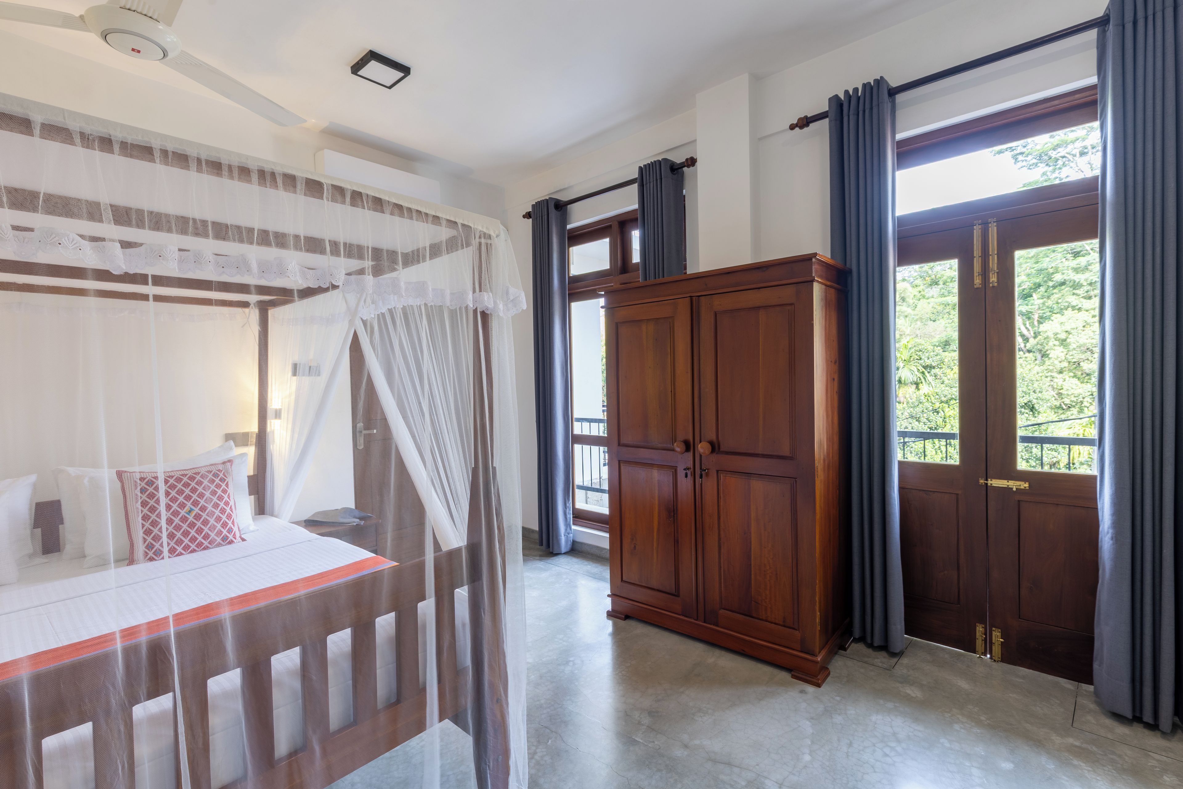 Un dormitorio con una cama con dosel, un armario de madera y un amplio ventanal con cortinas.