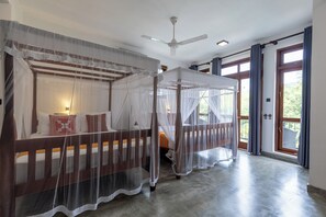 A room with two beds, each with a canopy, a ceiling fan, and a large window with curtains.