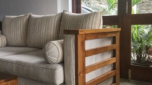 A grey sofa with wooden slats, positioned near a glass door leading to a garden with potted plants. - Hanthana House (Kandy)