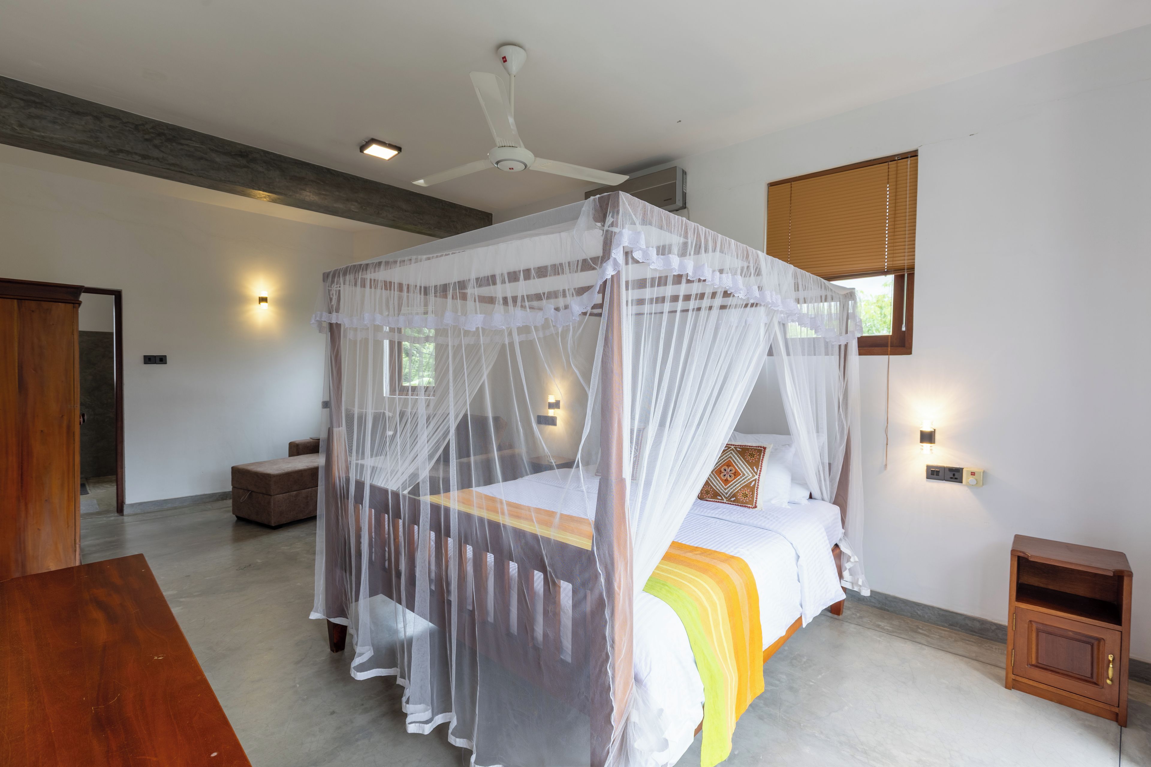 Ein Schlafzimmer mit Himmelbett, Deckenventilator und Fenster mit Jalousien.