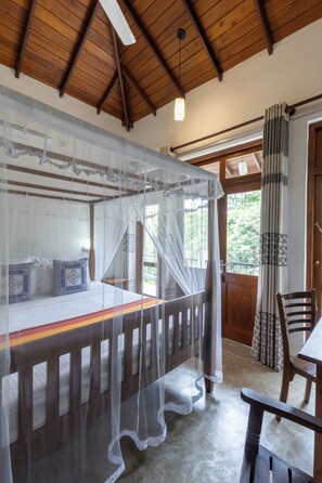 A room with a bed under a mosquito net, a wooden ceiling, a window with curtains, and a door with patterned curtains. - Hanthana House (Kandy)