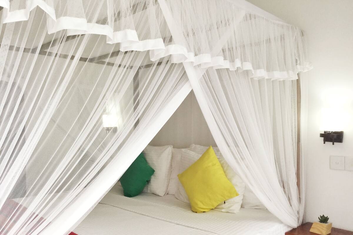 A bed with a white canopy and pillows in green and yellow.