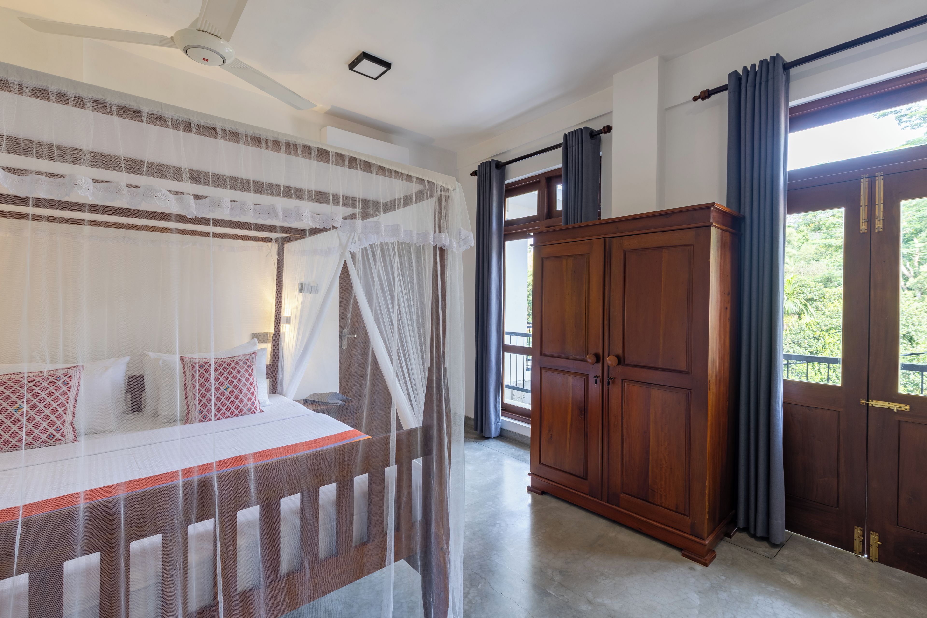 A bedroom with a four-poster bed, a wooden wardrobe, and a balcony with curtains.