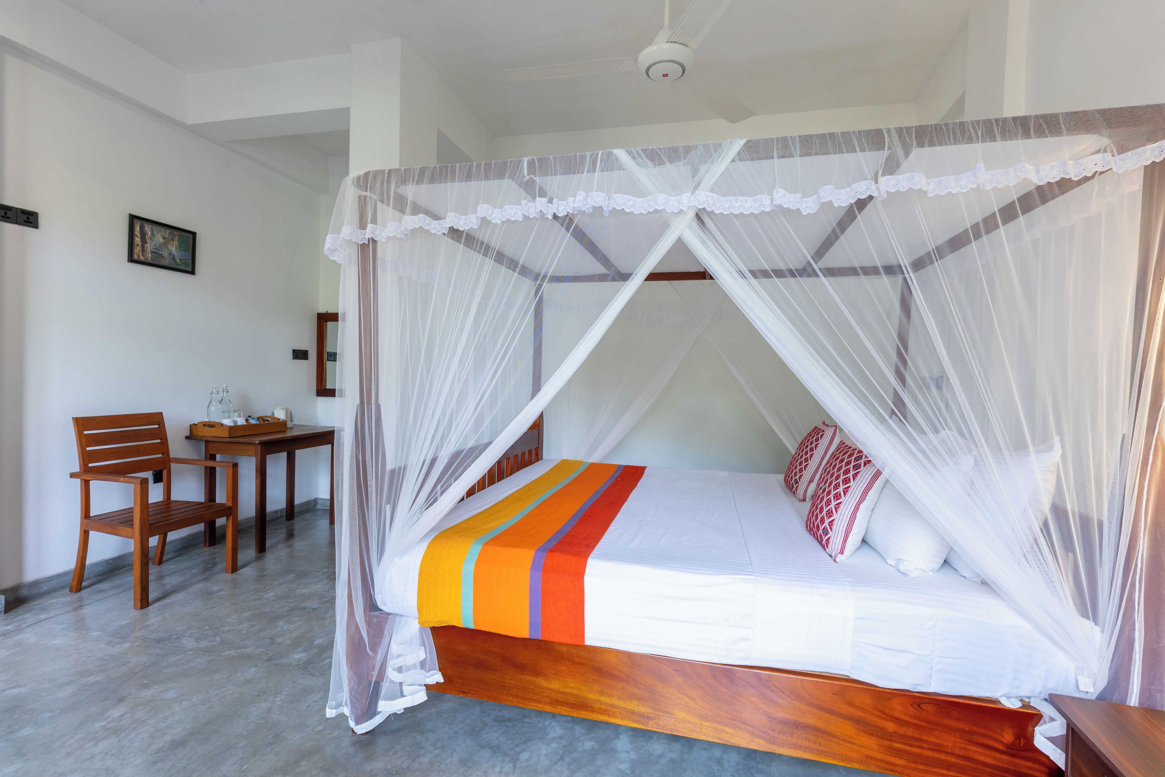 A room with a bed under a canopy, a desk with chairs, and a small table with items on it.
