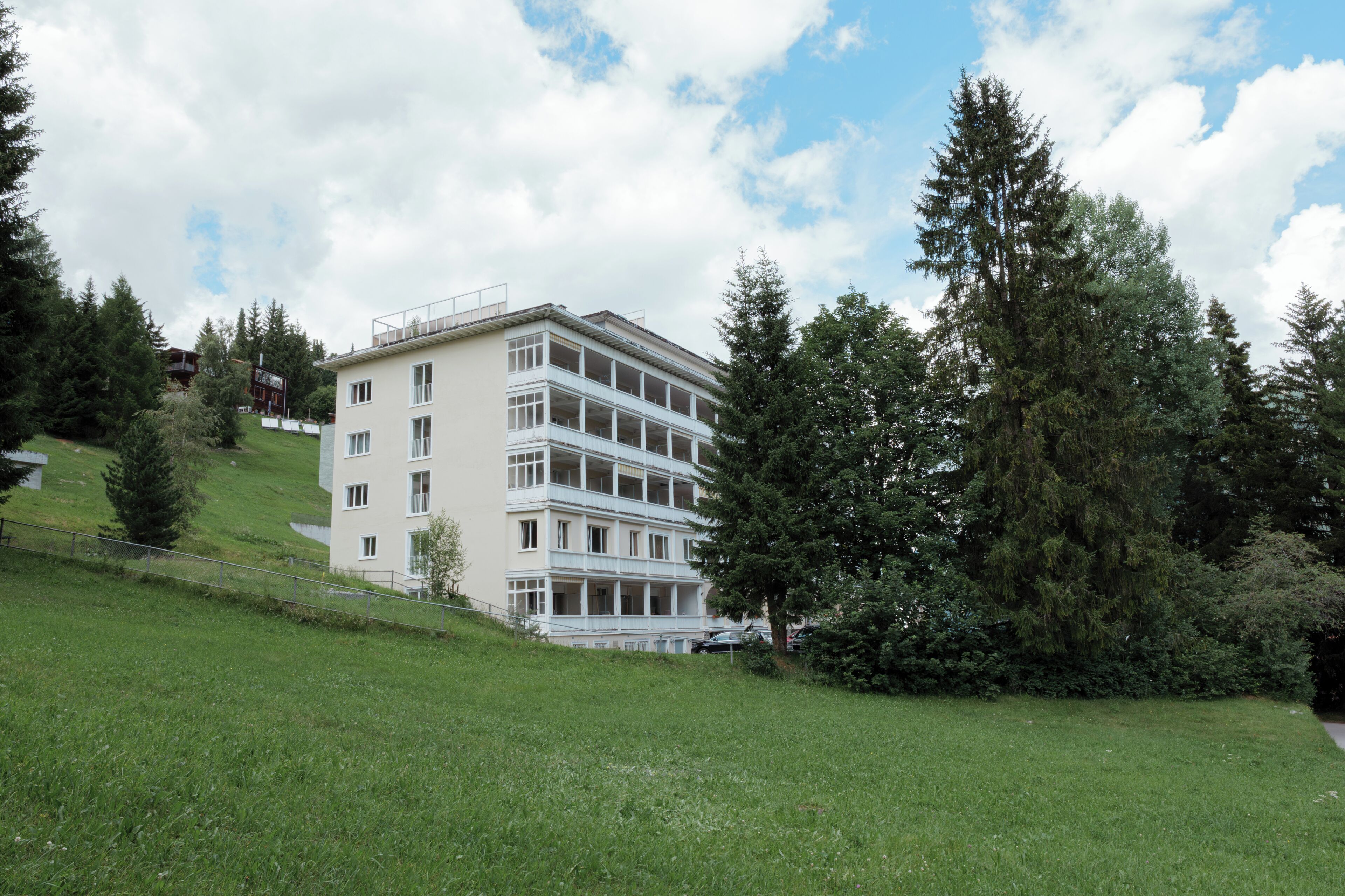 A multi-story building with a flat roof, surrounded by greenery and trees.