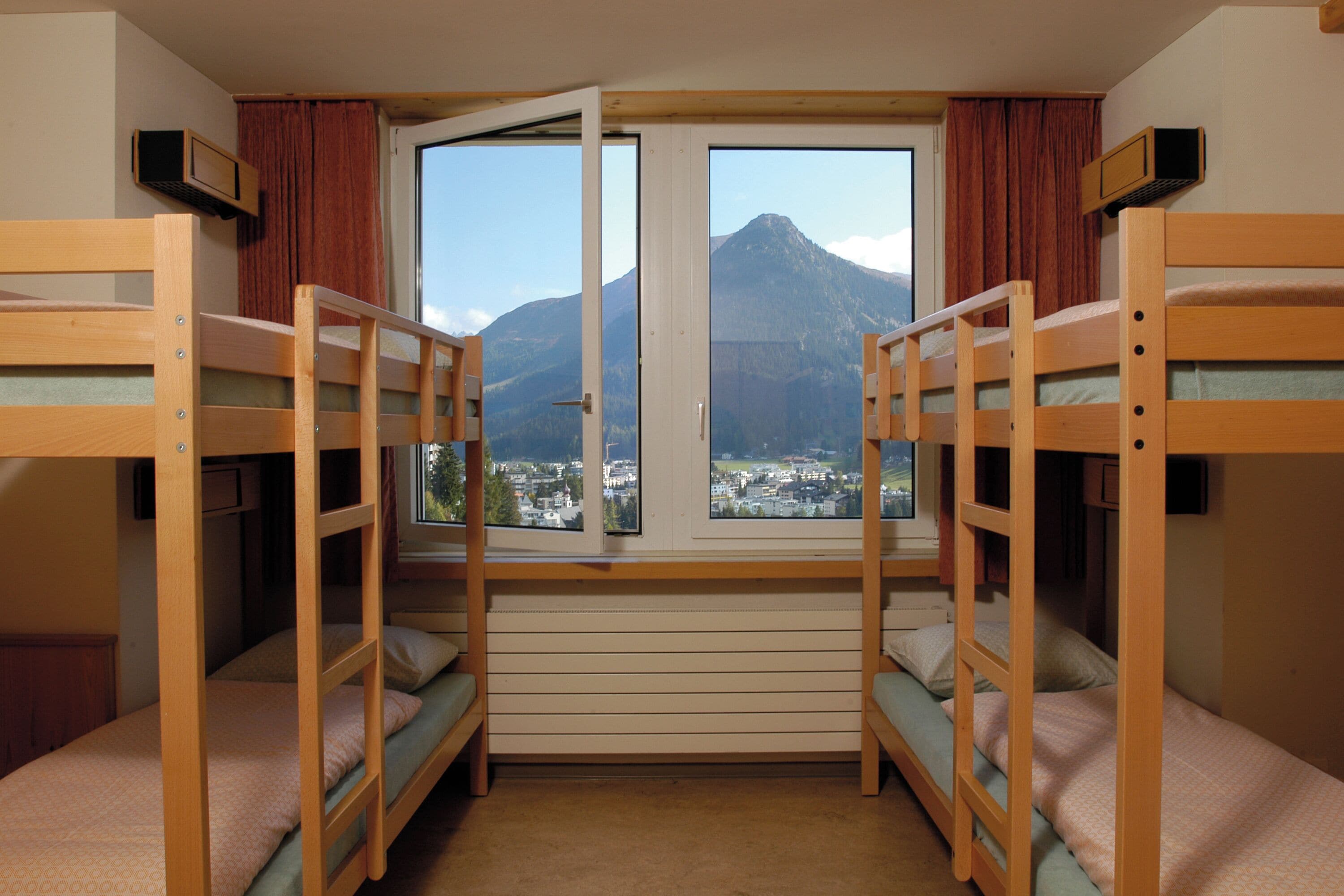 Een kamer met stapelbedden, een raam met uitzicht op een berg en een televisie aan de muur.