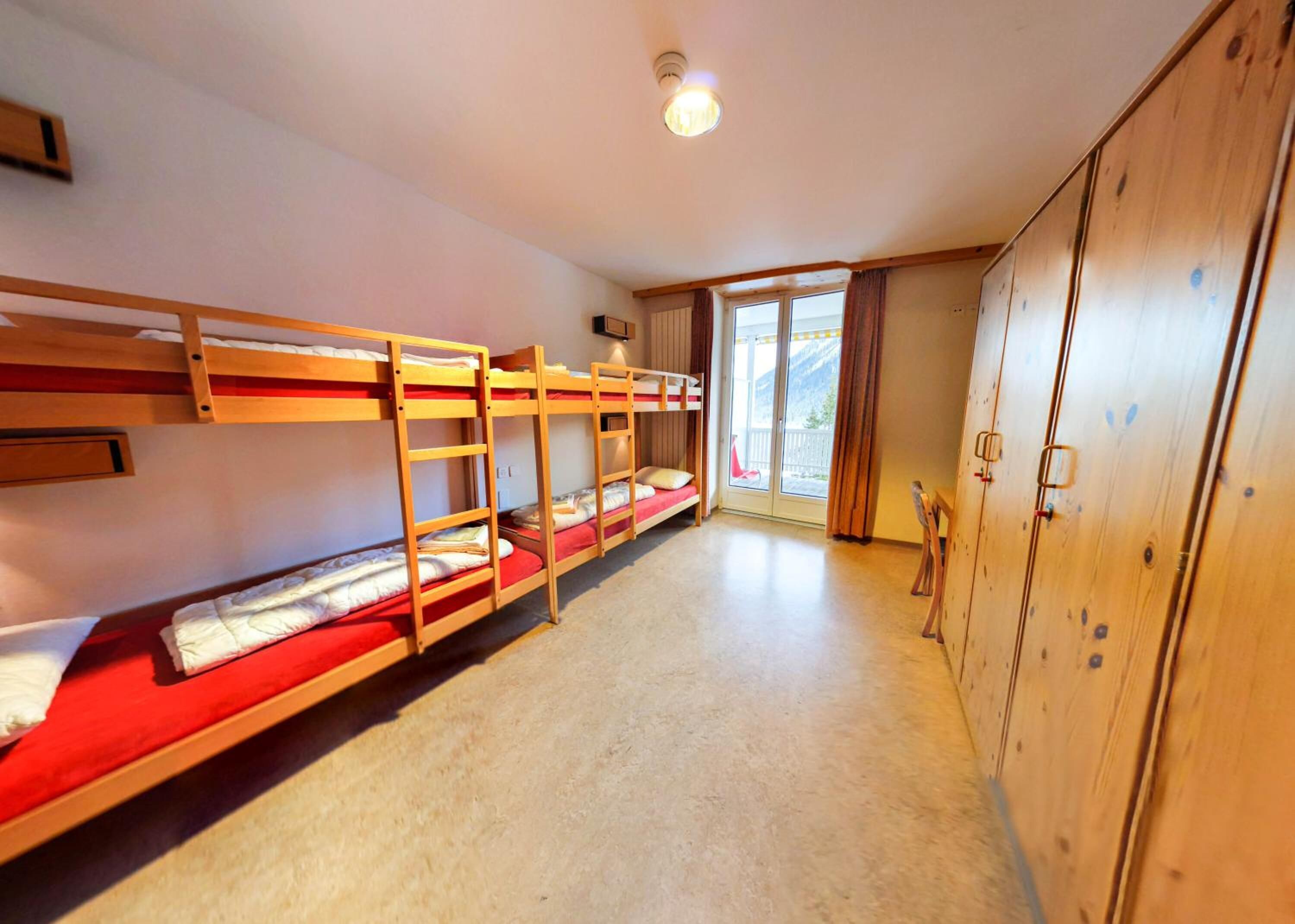 Ein Schlafsaalzimmer mit Etagenbetten, einer Schiebetür zu einem Balkon und einem Holzschrank.